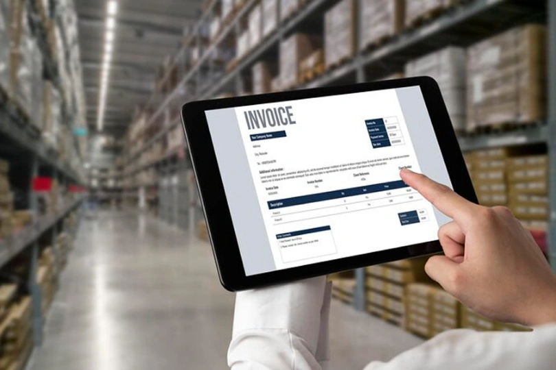 Person reviewing a digital invoice on a tablet inside a warehouse, showcasing automated invoice data extraction and integration with ERP systems for logistics companies using invoice capture software.